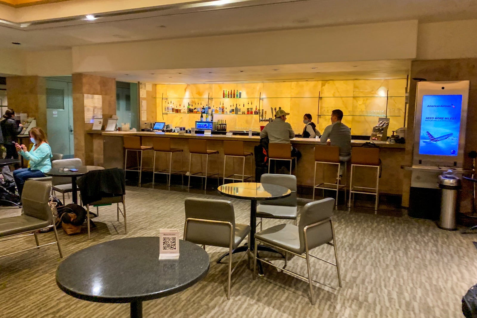 Interior of the American Airlines Admirals Club at DFW Terminal C with desks, armchairs, laptop users, and tarmac views